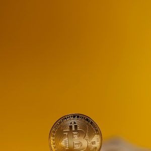 Close-up of a Bitcoin coin standing upright on a blurred yellow background, symbolizing digital finance.