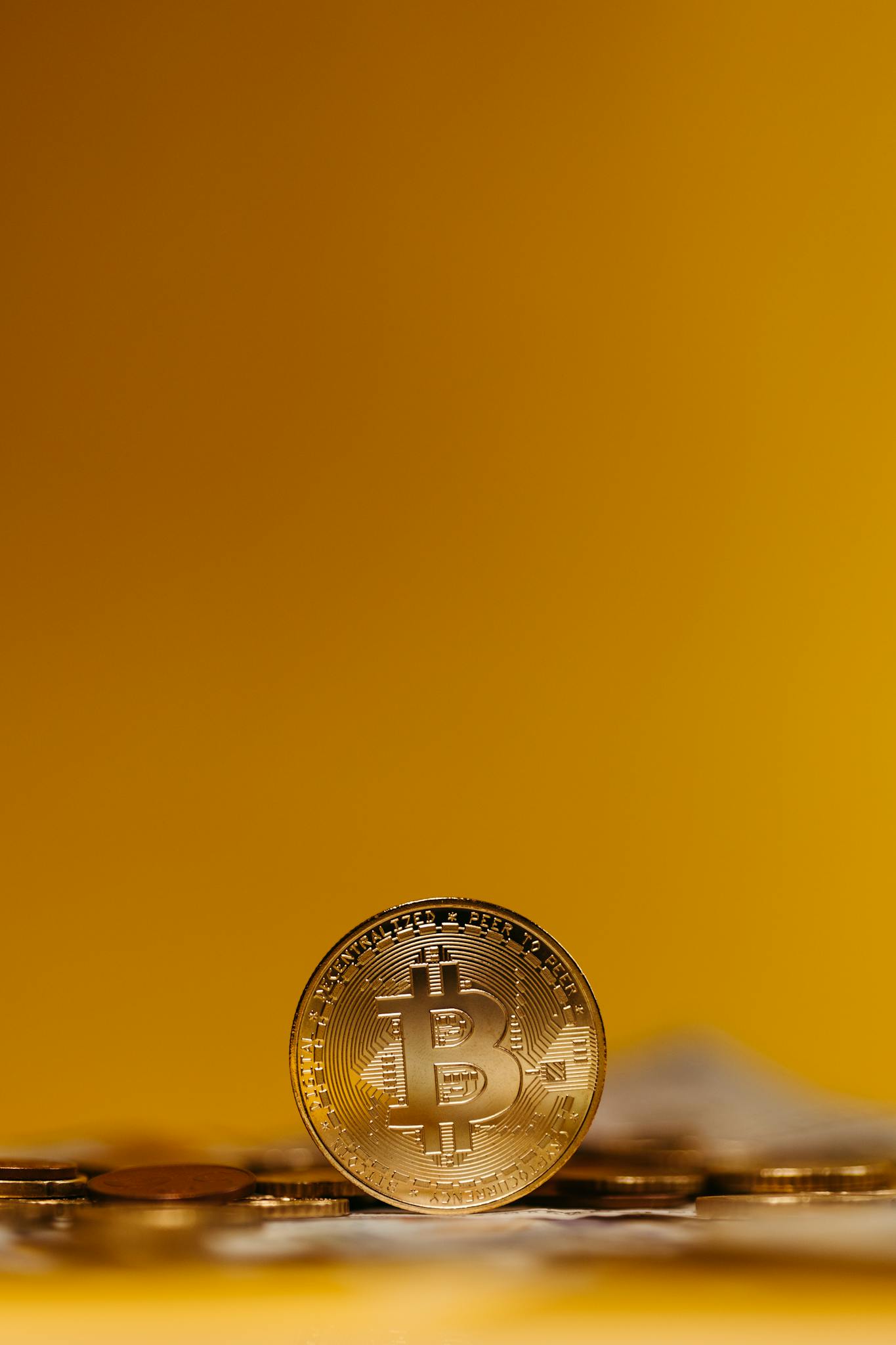 Close-up of a Bitcoin coin standing upright on a blurred yellow background, symbolizing digital finance.